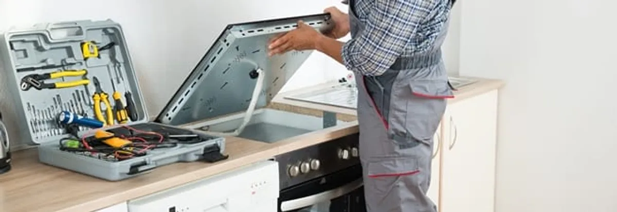 Cooktop repair technician lifting a built-in stovetop for service in Fort Collins, CO